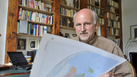 Wolfgang Lutz blättert in einem großen Atlas